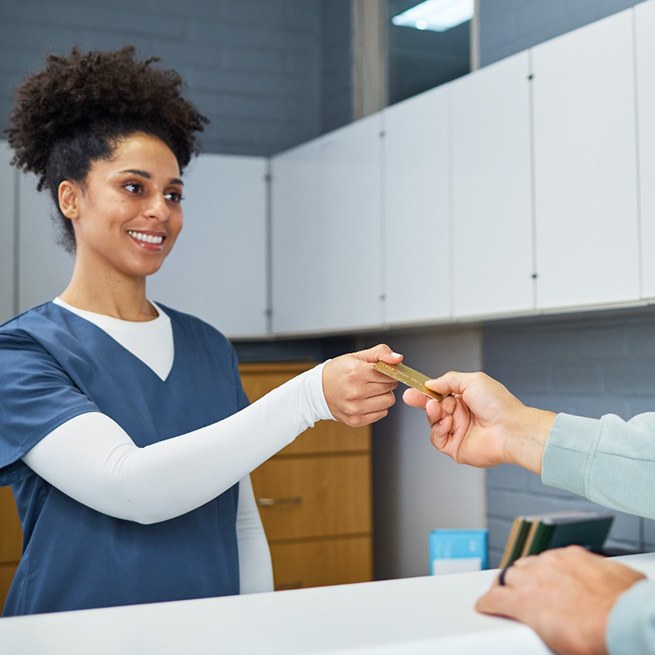 Man handing payment card at counter to woman in blue scrubs