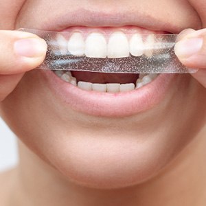 Someone applying whitening strip to their upper arch