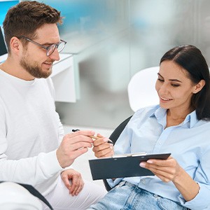 Man in white handing dental patient pen to fill out forms on clipboard
