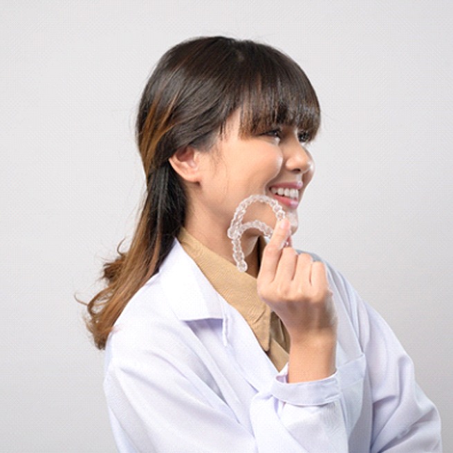 Woman looking to the side, holding two clear aligners in Burien