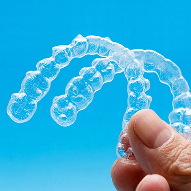 Hand holding two clear aligners against blue background