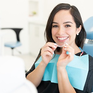 Woman in treatment chair smiling while holding clear aligner