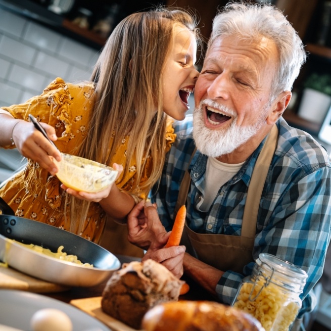 Older man with dental implant tooth replacement laughing with granddaughter