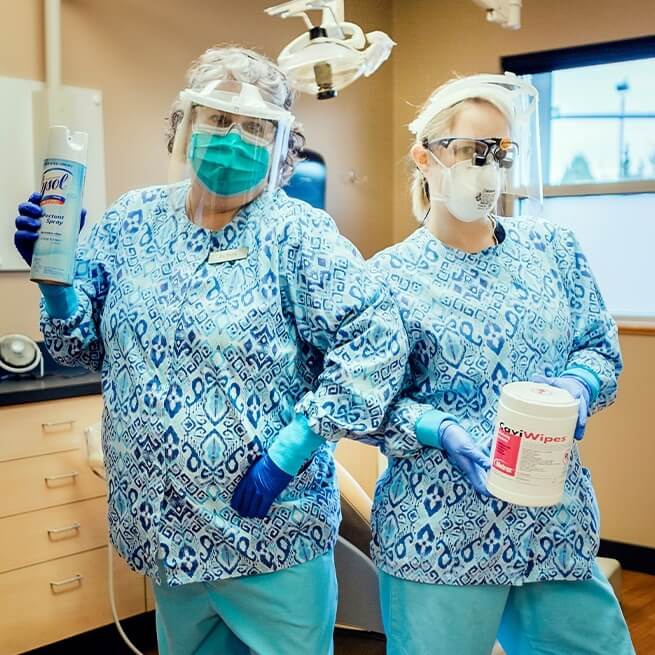 Burien dental team members wearing protective gear and holding cleaning supplies