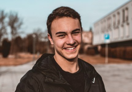 Young man in black jacket smiling outdoors