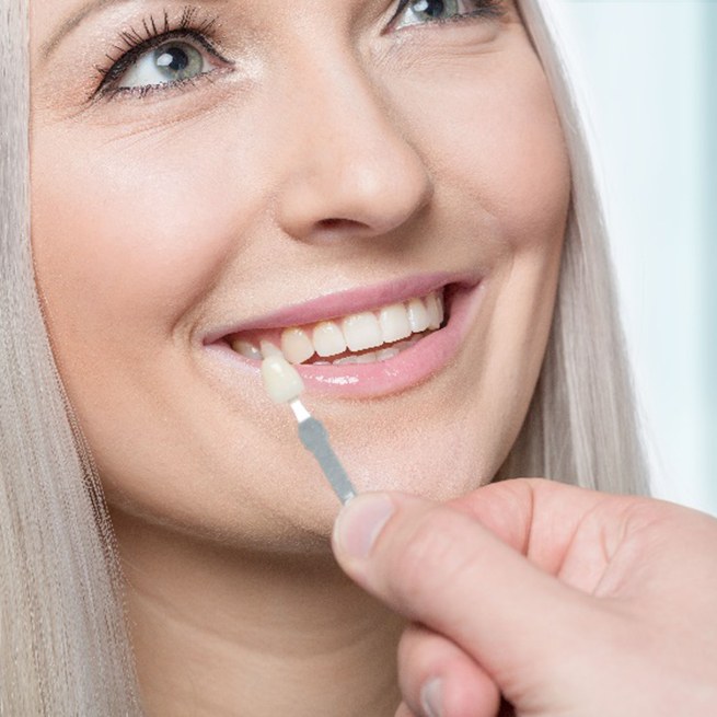 Young woman smiling while dentist shade-matches veneer