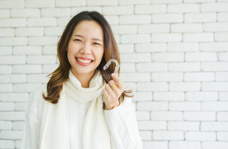 A woman holding a clear aligner and smiling.