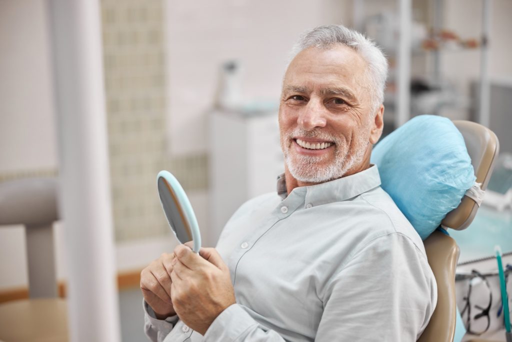 Man smiling while holding mirror in dentist's treatment chair