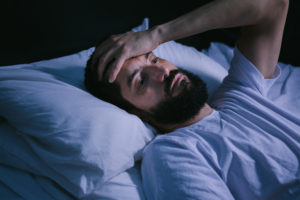 Tired man in bed at night holding head