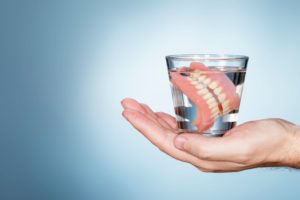 Hand holding a glass of water with dentures