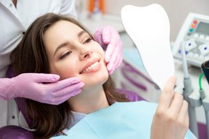 Woman in dental chair smiling into mirror with dentist touching her chin